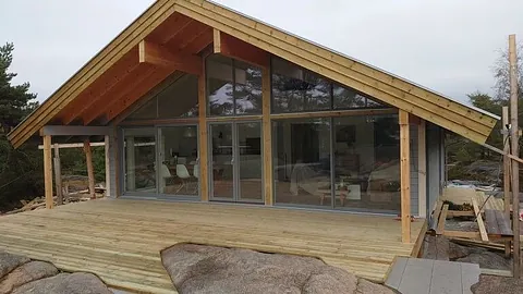 Ferdigbygd hytte med stor terrasse og store glassvinduer mot naturen.