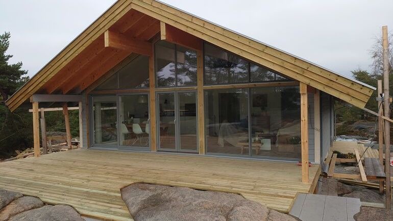 Ferdigbygd hytte med stor terrasse og store glassvinduer mot naturen.