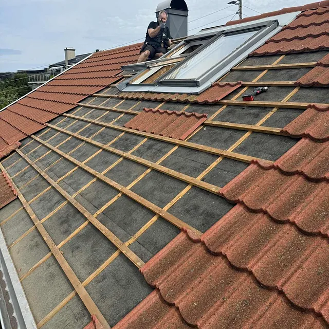 Tømrer jobber med vindusinstallasjon på skråtak med røde takstein.