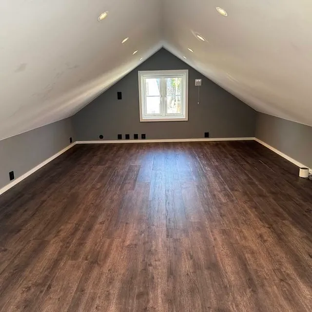 Nymalt loftsrom med mørkt gulv, skråtak og innfelt belysning.