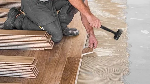 Håndverker legger parkett med lim og gummiklubbe på nytt gulv.