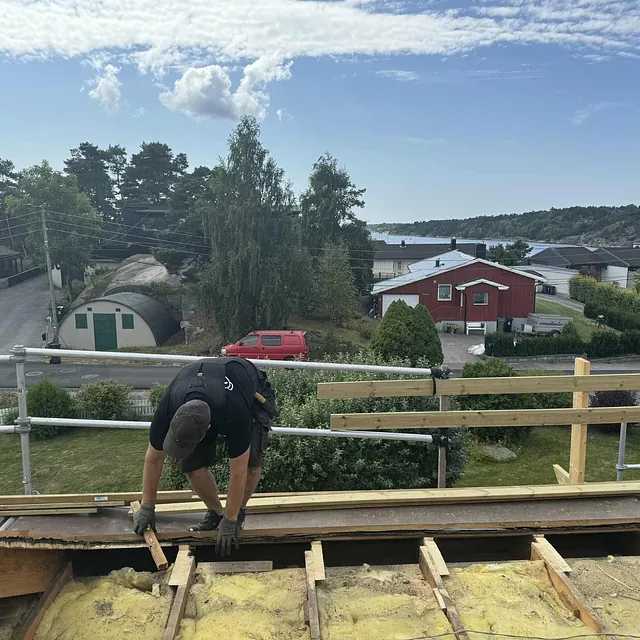 Tømrer jobber med etterisolering og lekting på tak med havutsikt.