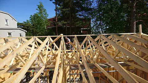 Hytte med steinpeis og terrasse, byggearbeid pågår utendørs.