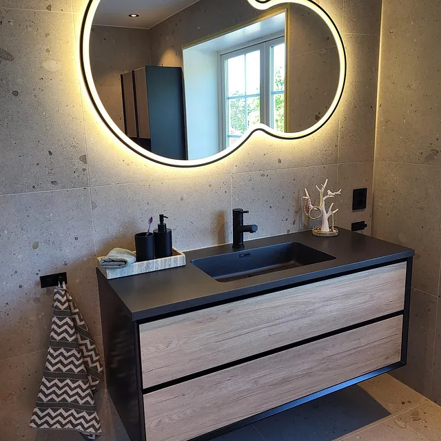 Moderne baderom med speil med lys, servant og grå fliser.