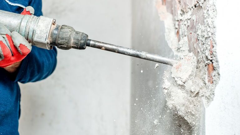 Håndverker bruker borhammer for å rive betongvegg innendørs.